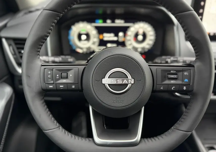 Vue rapprochée du volant cuir noir du Nissan Qashqai 2025 avec commandes intégrées et tableau de bord numérique flou.