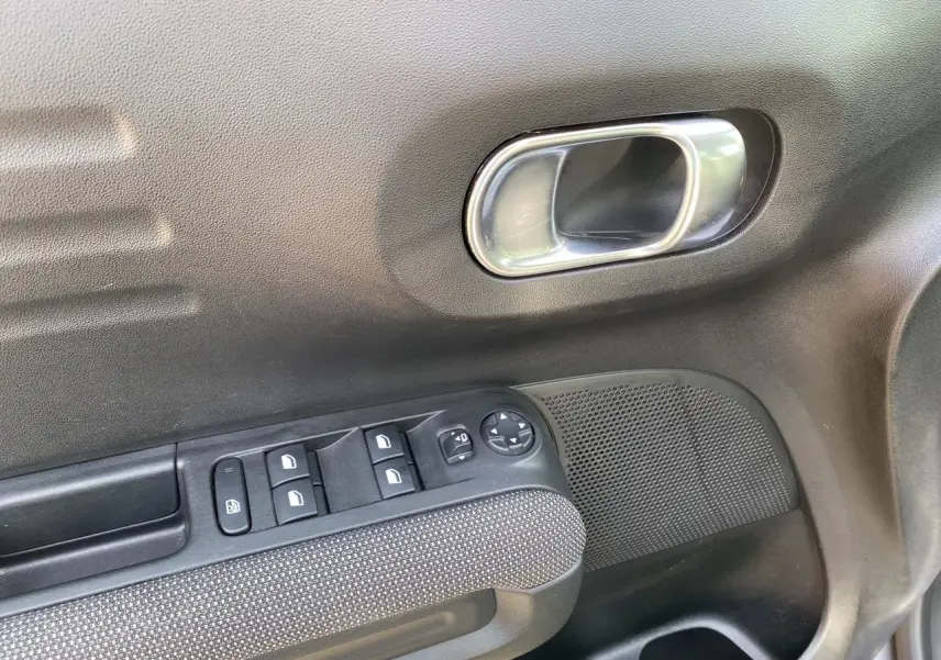 Gros plan sur la porte côté conducteur de la Citroën C3 Aircross gris platinium, montrant les commandes des vitres et la poignée intérieure.