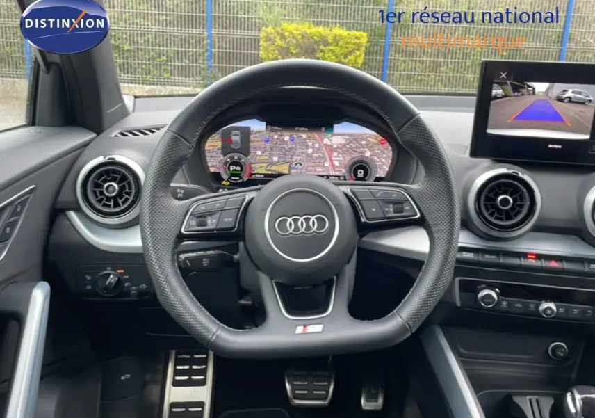 Vue intérieure centrée sur le volant Audi S-Line avec tableau de bord digital et écran de caméra de recul.
