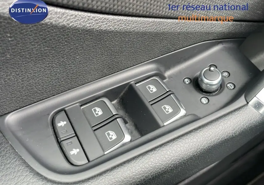 Gros plan sur les commandes de lève-vitres et réglage des rétroviseurs côté conducteur d’un Audi Q2 argent rose métal.