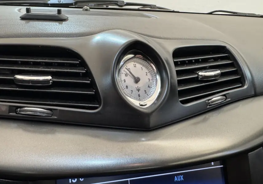Gros plan sur l'horloge centrale et les aérateurs noirs du tableau de bord gris d'une Maserati Granturismo S 4.7 2010.