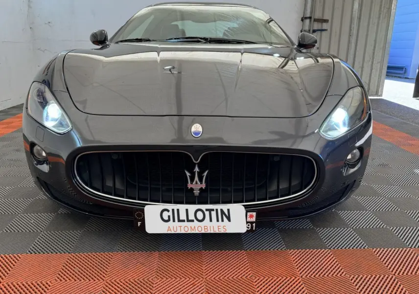 Vue avant rapprochée d'une Maserati Granturismo S 4.7 gris foncé avec phares allumés et calandre imposante.
