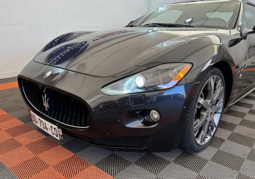 Vue 3/4 avant droit d'une Maserati Granturismo S 4.7 gris foncé avec phares bi-xénon allumés et jantes alliage.
