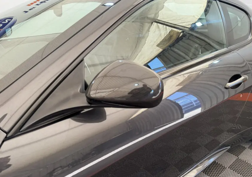 Vue rapprochée du côté gauche d'une Maserati Granturismo S 4.7 gris foncé, mettant en valeur le rétroviseur carbone.