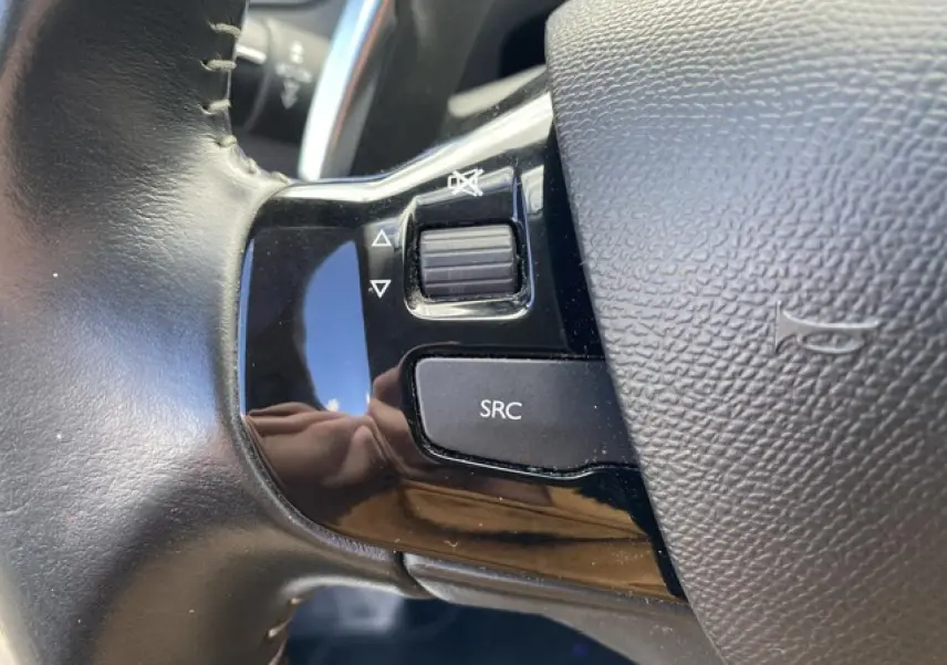 Gros plan sur les commandes audio au volant noir du Peugeot 308 SW gris Hurricane, avec bouton SRC et molette de volume.