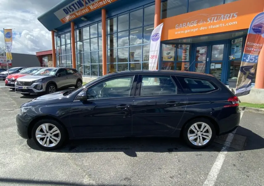 Profil côté gauche d'une Peugeot 308 SW gris hurricane garée devant un garage avec jantes alliage 16 pouces.