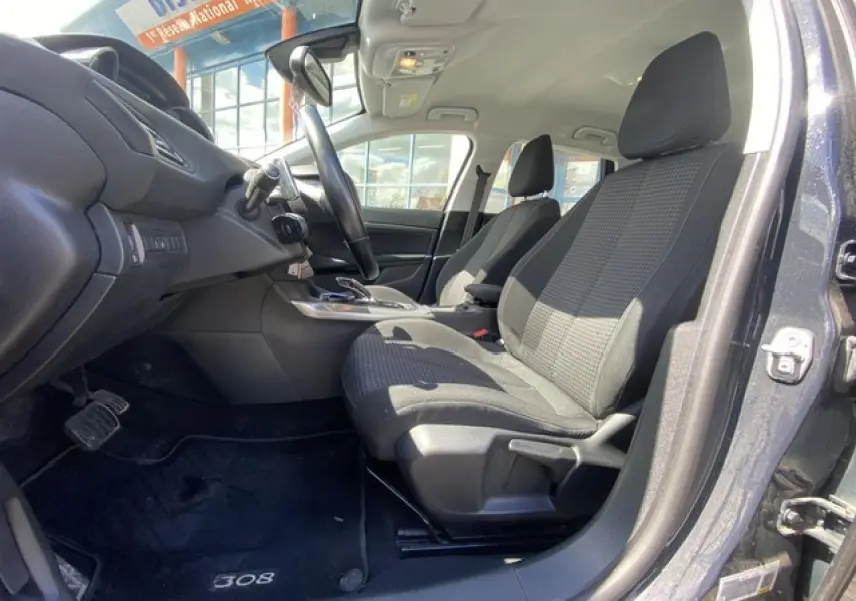 Vue intérieure côté conducteur de la Peugeot 308 SW 2018 gris hurricane, sièges tissu noir et tableau de bord moderne.