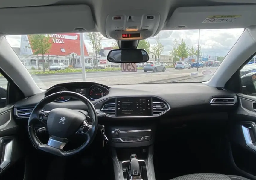 Vue intérieure avant du tableau de bord et volant noir de la Peugeot 308 SW gris Hurricane avec écran tactile central.