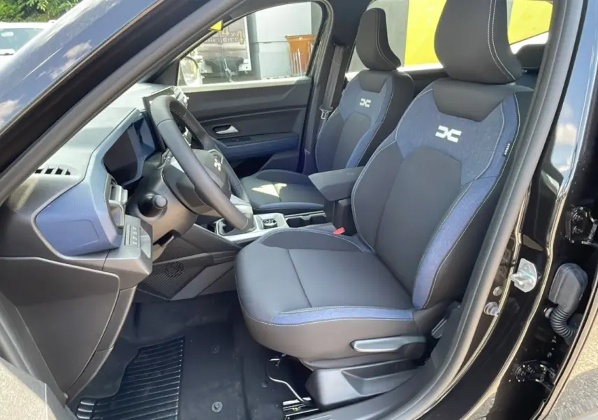 Intérieur du Dacia Bigster TCE 130 4x4 Expression Plus 2025, sièges avant noirs et bleus avec logo DC visibles côté conducteur.