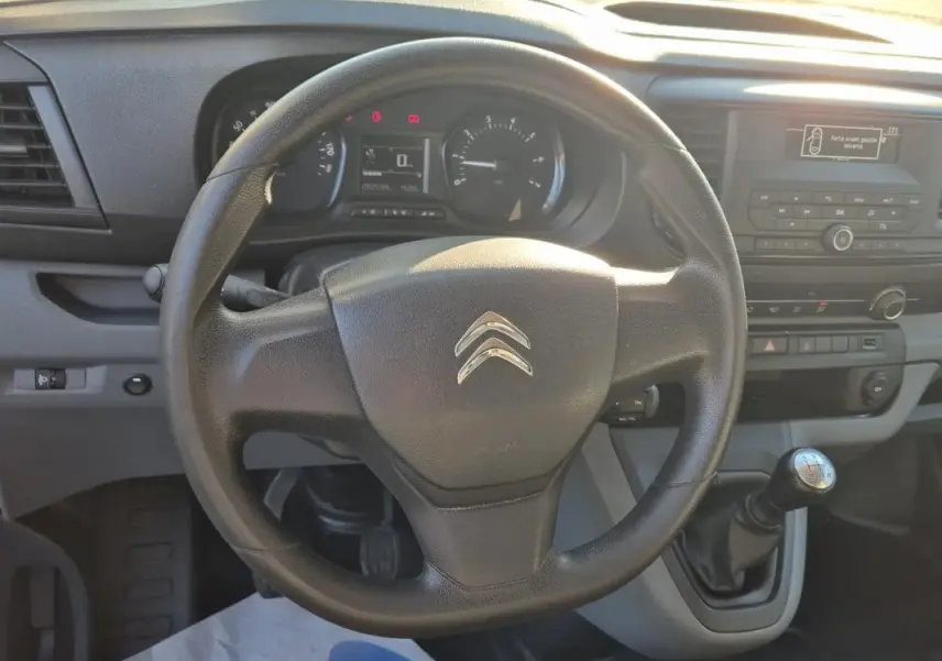 Vue intérieure centrée sur le volant Citroën et levier de vitesse manuel du Jumpy blanc, tableau de bord et console visibles.