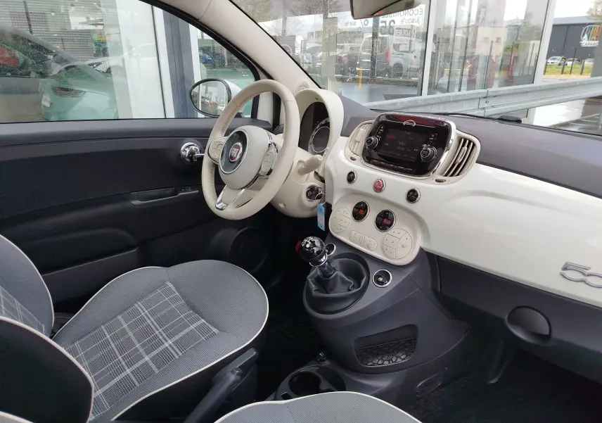 Vue intérieure côté conducteur de la Fiat 500 Lounge blanche, avec tableau de bord crème et volant assorti.
