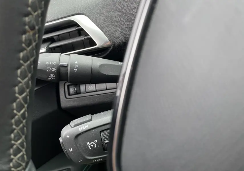 Détail du commodo de régulateur de vitesse et des commandes d'éclairage à gauche du volant dans un Peugeot 3008 gris platinium.