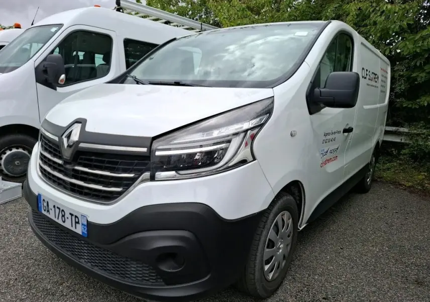 Renault Trafic Fourgon blanc vu en 3/4 avant droit avec marquage commercial sur la porte latérale droite.