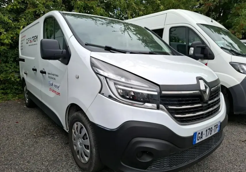 Renault Trafic Fourgon blanc vu en 3/4 avant droit, avec logo et marquage commercial sur la porte côté gauche.