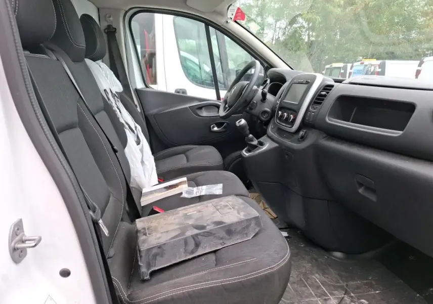Intérieur du Renault Trafic Fourgon blanc vu côté conducteur, montrant les sièges noirs et le tableau de bord moderne.