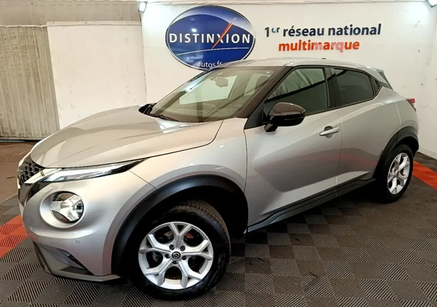 Nissan Juke gris clair en 3/4 avant droit, avec rétroviseurs ton caisse et jantes alliage visibles.