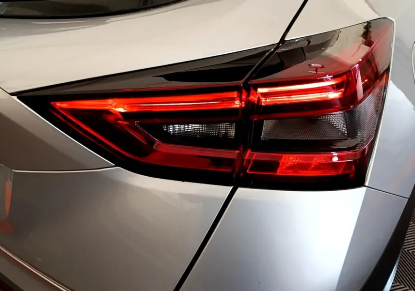 Gros plan sur le feu arrière droit rouge et noir d’un Nissan Juke gris clair, version 2022, avec carrosserie lisse.