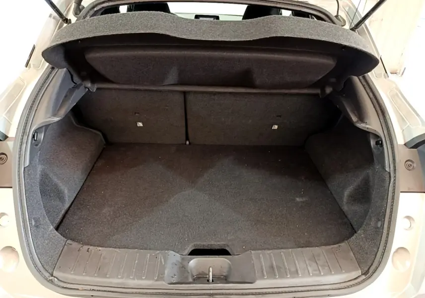 Coffre ouvert vu de l'arrière d'un Nissan Juke gris clair, montrant l'espace de chargement vide et la tablette de coffre relevée.
