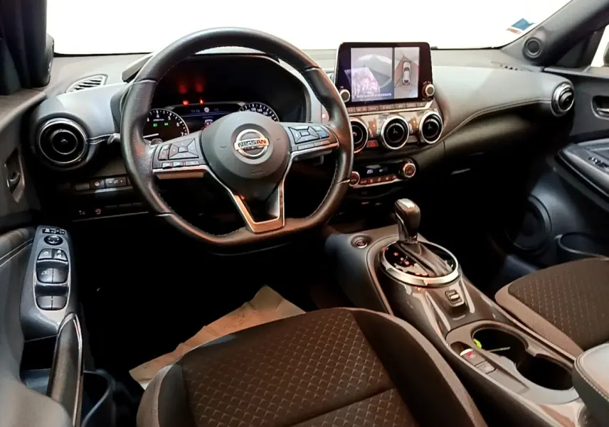 Vue intérieure avant du Nissan Juke 2022 avec volant cuir, écran tactile central et levier de boîte automatique.