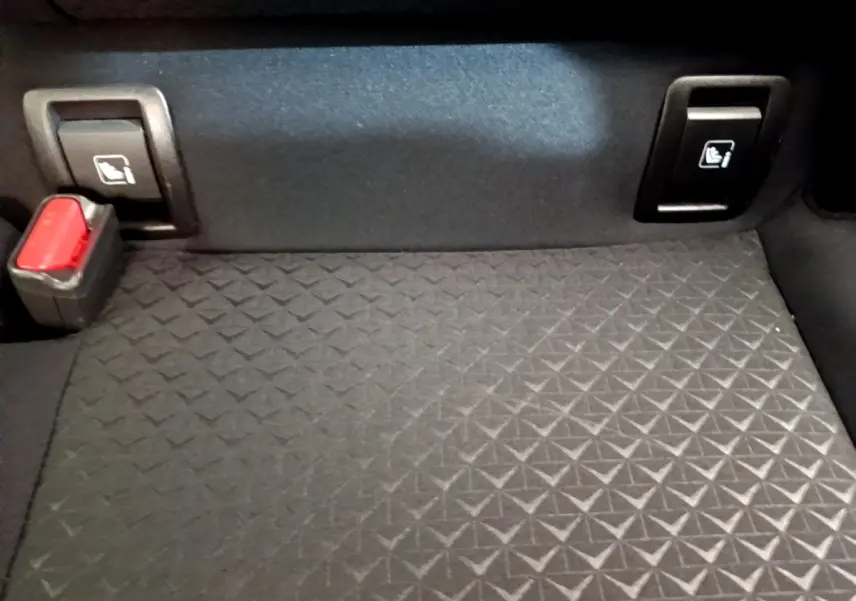 Détail du coffre noir du Nissan Juke 2022 avec boutons de rabattement des sièges arrière et boucle de ceinture rouge.