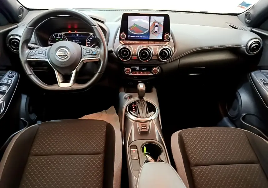 Vue intérieure frontale du tableau de bord et volant cuir noir du Nissan Juke 2022 avec écran tactile et boîte automatique.