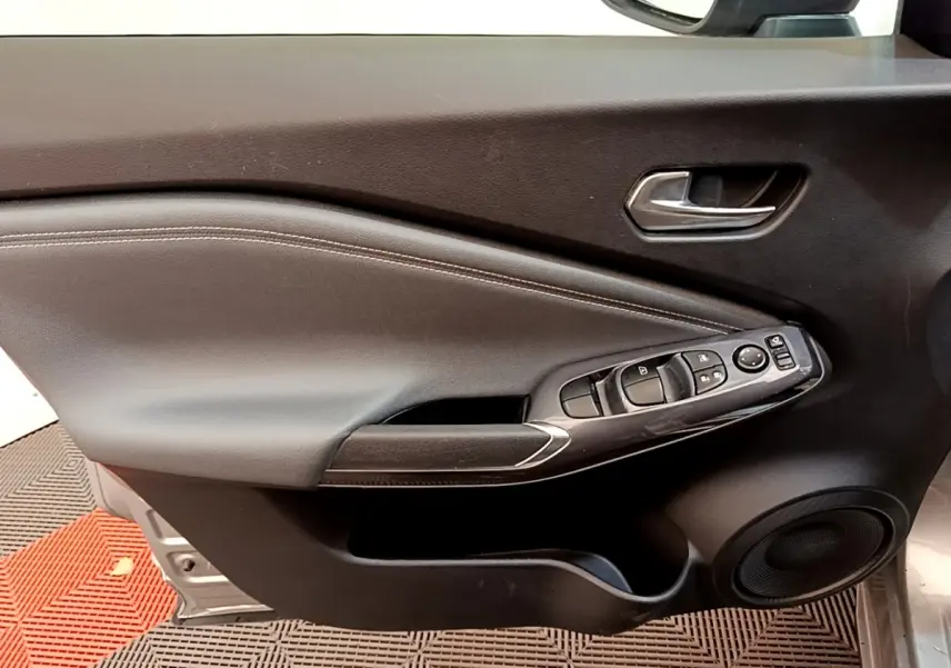 Vue rapprochée de la porte avant gauche du Nissan Juke gris clair 2022, avec commandes électriques et poignée intégrée.