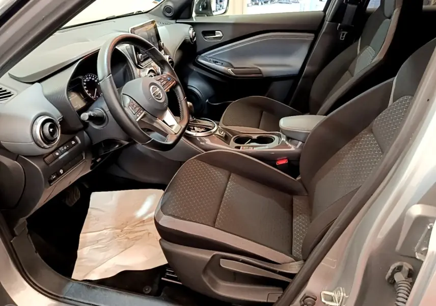 Vue intérieure côté conducteur du Nissan Juke gris clair 2022, montrant sièges et tableau de bord avec écran tactile.