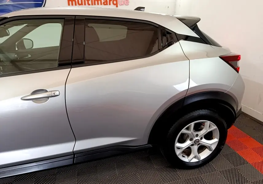 Vue latérale côté droit d'un Nissan Juke gris clair avec jante alliage et poignées ton caisse.