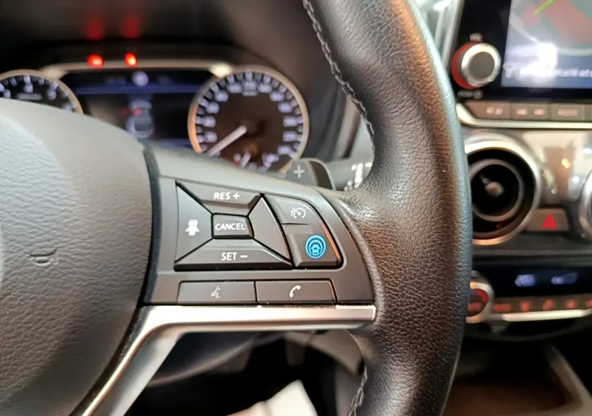 Gros plan sur le volant en cuir noir du Nissan Juke 2022 avec commandes multifonctions et tableau de bord flou en arrière-plan.