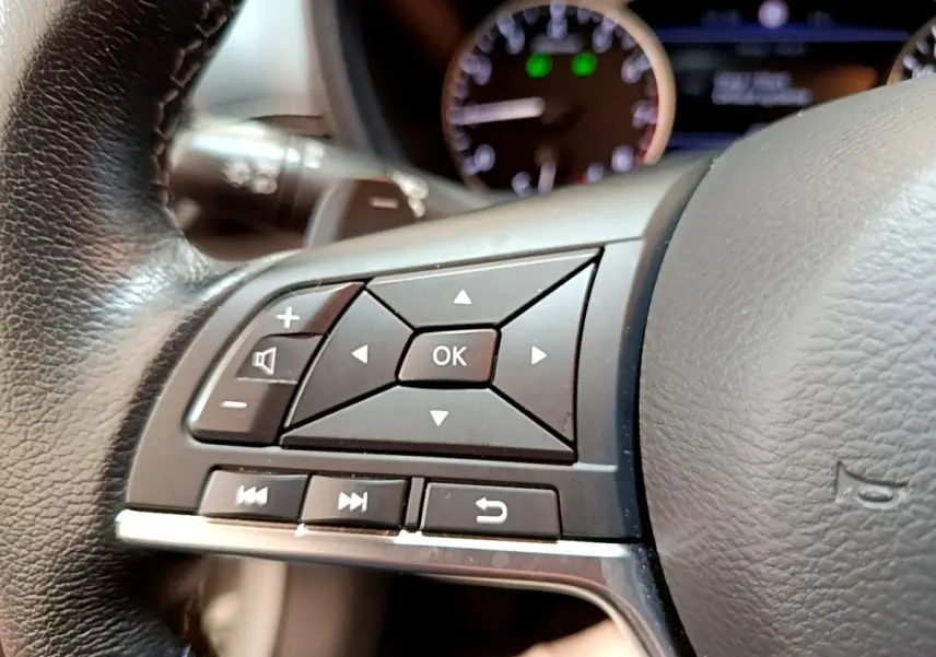 Gros plan sur les commandes au volant en cuir noir du Nissan Juke gris clair, avec tableau de bord flou en arrière-plan.