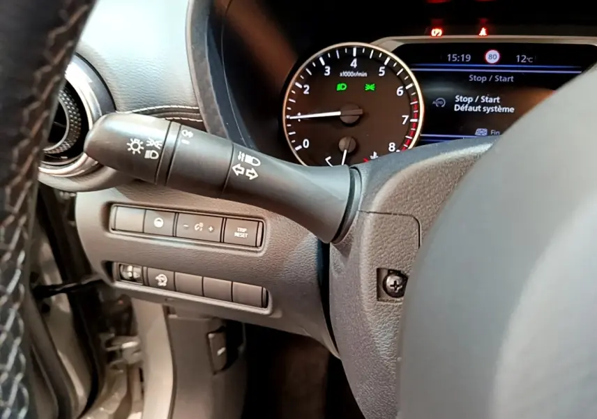 Détail du tableau de bord et commodo gauche du Nissan Juke 2022 essence, affichage multifonctions et compte-tours visibles.