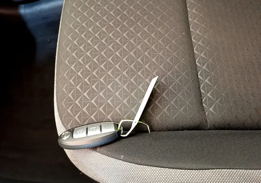 Clé de voiture Nissan Juke posée sur la banquette arrière en tissu gris foncé avec motif géométrique.