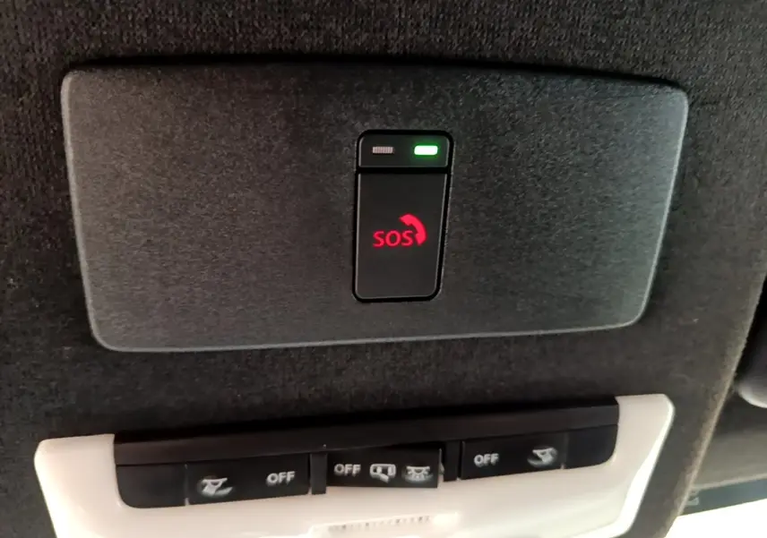 Gros plan sur le bouton SOS rouge et les commandes d’éclairage intégrées au plafond intérieur du Nissan Juke gris clair.