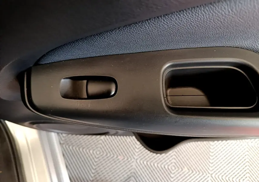 Gros plan sur la poignée intérieure noire de porte avant d'un Nissan Juke gris clair, vue côté conducteur.