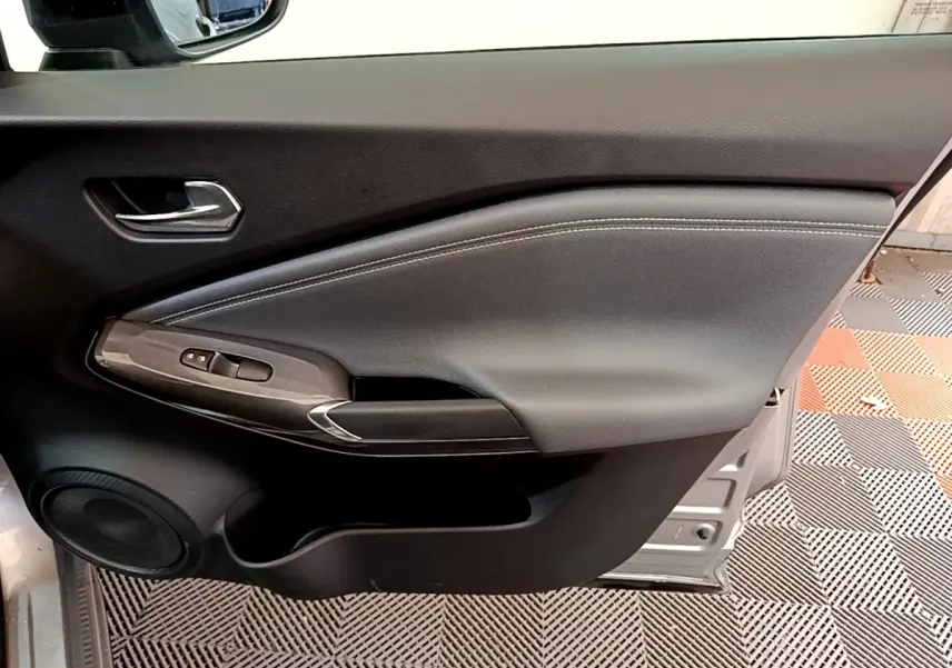 Vue intérieure côté gauche de la porte avant d’un Nissan Juke gris clair, avec commandes électriques et haut-parleur intégré.