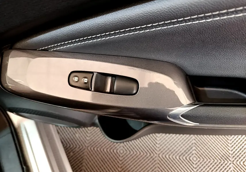 Gros plan sur la commande de verrouillage des portes côté conducteur du Nissan Juke gris clair, avec garniture cuir noire.