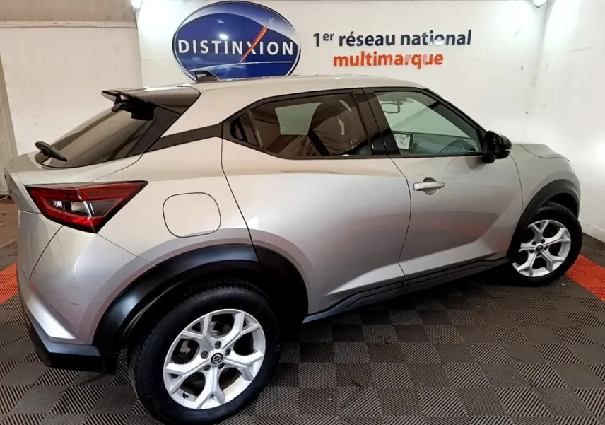 Nissan Juke gris clair vu de profil droit, avec toit noir et jantes alliage cinq branches, en intérieur showroom.
