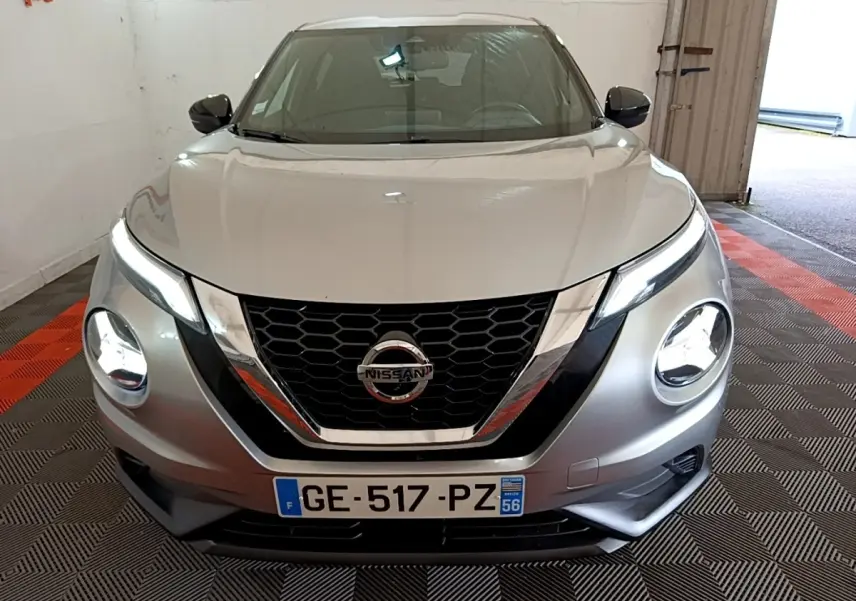 Vue avant d'un Nissan Juke gris clair 2022 avec phares LED allumés et calandre chromée en intérieur garage.