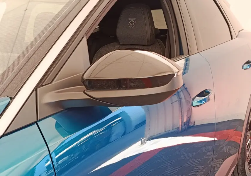 Vue rapprochée du rétroviseur côté gauche d’un Peugeot 3008 bleu 2025 avec siège avant et logo Peugeot visible.