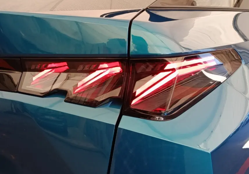 Gros plan sur les feux arrière allumés du Peugeot 3008 bleu, soulignant les lignes anguleuses et modernes du coffre.