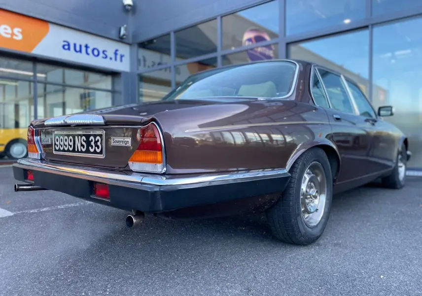Vue 3/4 arrière droite d'une Jaguar XJ6 Série 3 4.2 Sovereign marron de 1985 avec plaques françaises et feux caractéristiques.