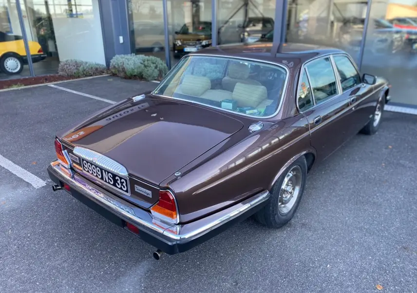 Vue 3/4 arrière droite d'une Jaguar XJ6 Série 3 4.2 Sovereign marron de 1985 avec détails chromés et intérieur clair visible.