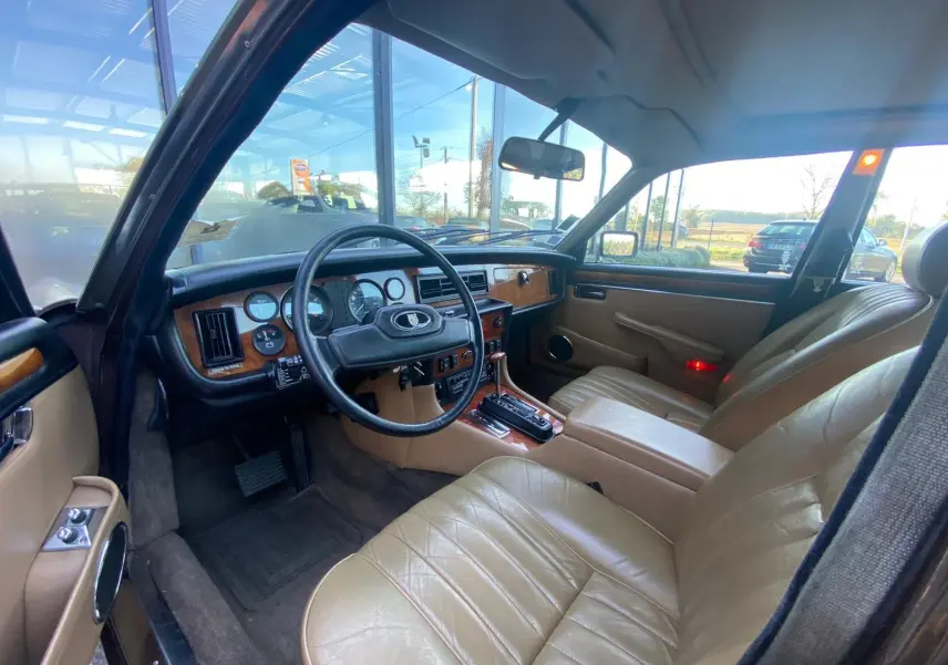 Intérieur beige du Jaguar XJ6 Série 3 4.2 Sovereign 1985, vue côté conducteur avec tableau de bord en bois et volant noir.