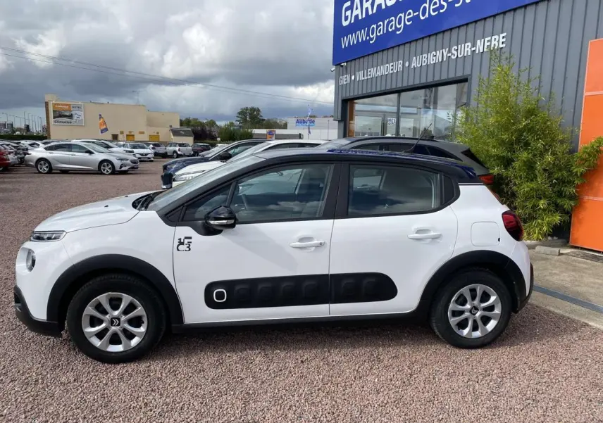 Profil côté gauche d'une Citroën C3 blanche avec toit noir, protections latérales noires et jantes alliage 15 pouces.