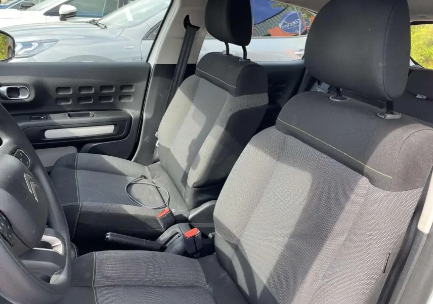 Intérieur avant de la Citroën C3 blanche 2019, vue côté gauche montrant les sièges tissu gris et le volant.