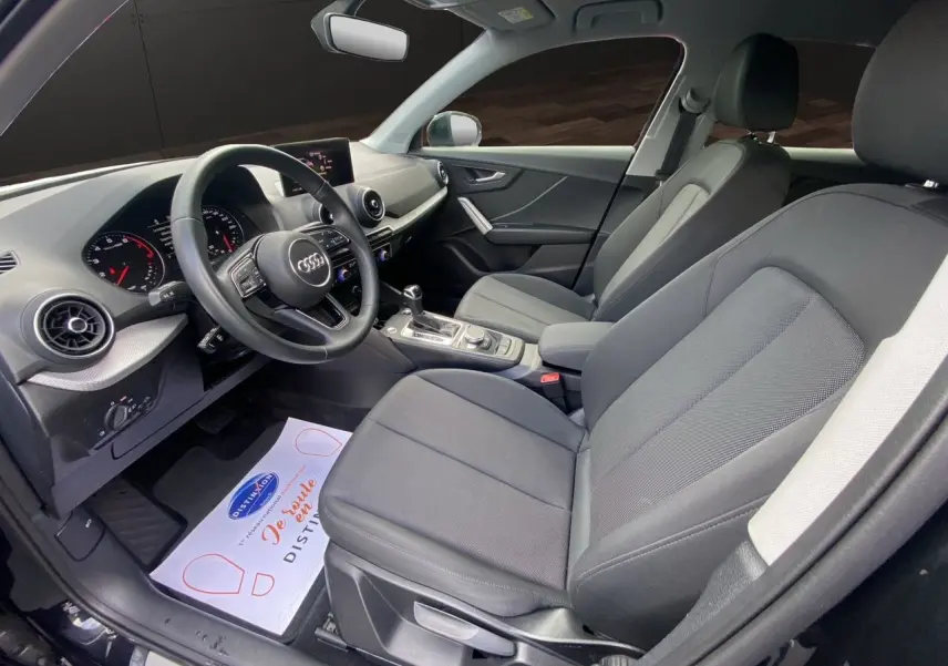Intérieur avant de l'Audi Q2 35 TFSI 2023 en tissu noir, vue côté conducteur avec tableau de bord et volant visibles.
