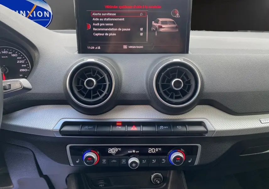 Tableau de bord intérieur d'Audi Q2 2023 avec écran central affichant aides à la conduite et commandes climatisation.
