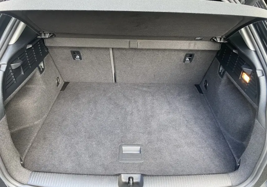 Coffre spacieux ouvert d’un Audi Q2 noir Mito, montrant la moquette grise et les fixations Isofix arrière.