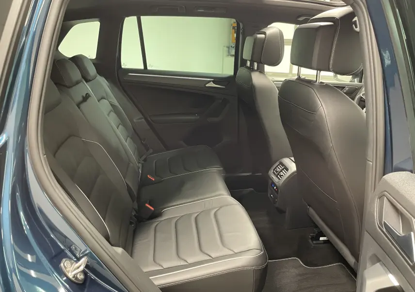 Vue intérieure côté gauche du Volkswagen Tiguan 2024 Nightshade Blue, montrant la banquette arrière en cuir noir avec surpiqûres blanches.