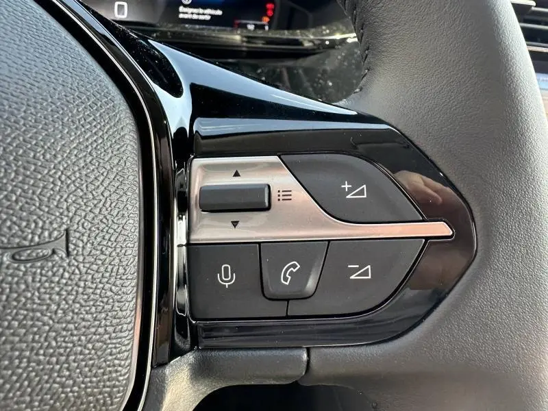 Gros plan sur les commandes du volant côté gauche de la Peugeot 308 2025, boutons noirs et argentés intégrés au cuir gris.